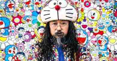 Takashi Murakami smiling in front of one of his colorful art pieces